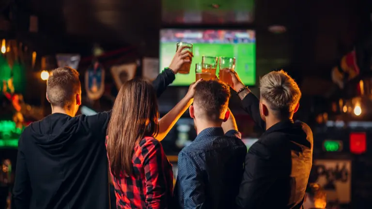 Teknisa - Sistema para bar: Pessoas brindando assistindo um jogo de esporte dentro do bar