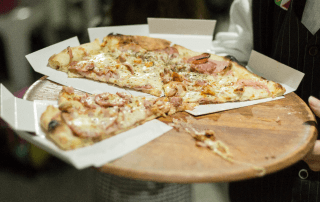 Close de um garçom segurando uma bandeja de madeira com fatias de pizza de calabresa em um restaurante com rodízio.