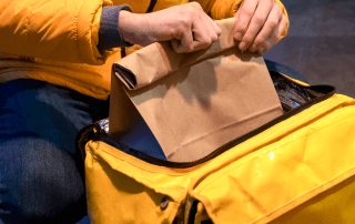 Entregador de delivery com jaqueta amarela fechando um saco de papel dentro de uma bolsa térmica de entrega.