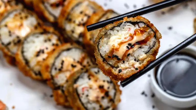 Close-up de um prato de hot roll (sushi frito) em um rodízio japonês, com hashis (palitos) segurando uma peça sobre um molho shoyu.