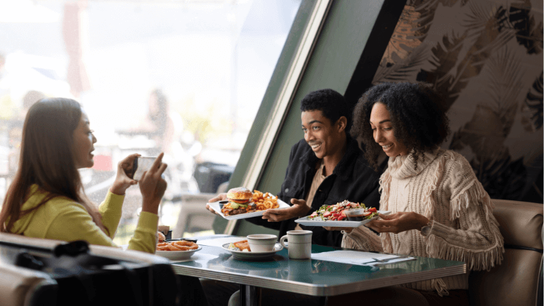 Cliente tirando foto de hambúrguer e salada com o celular em uma mesa com amigos para marketing de restaurantes.