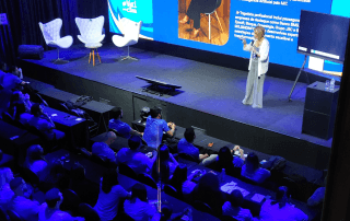 Palestrante no palco do TekWeek 2026 apresentando para uma plateia em um auditório moderno com iluminação azul.