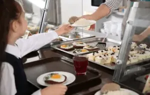 Criança recebendo refeição em refeitório escolar durante a distribuição da merenda em escola pública e com gestão do sistem Teknisa.
